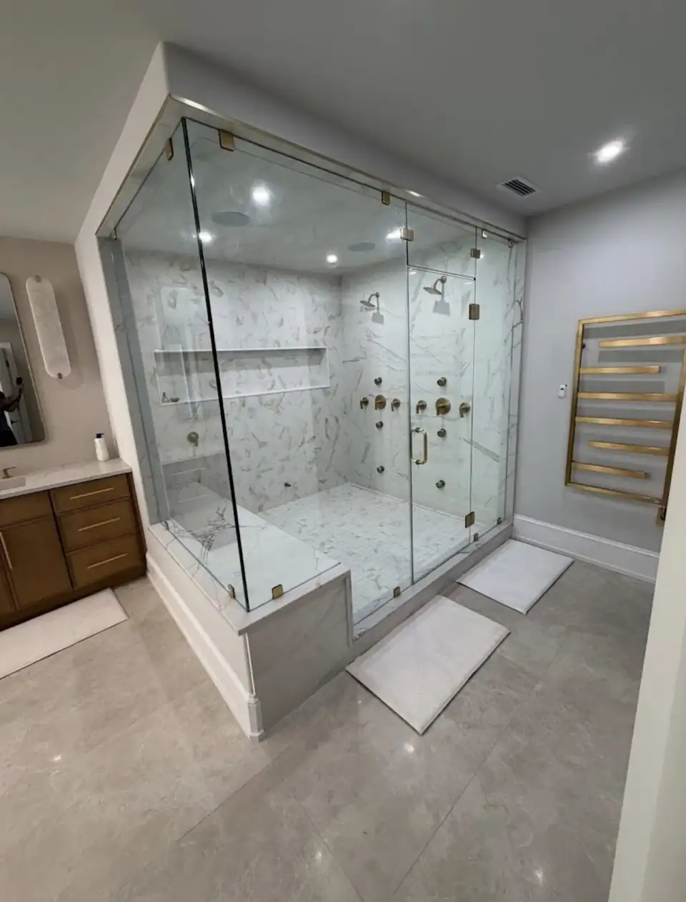 Bathroom remodeling in Dallas-Fort Worth: glass-enclosed marble-look shower with several shower heads, a tiled bench and a brass towel warmer