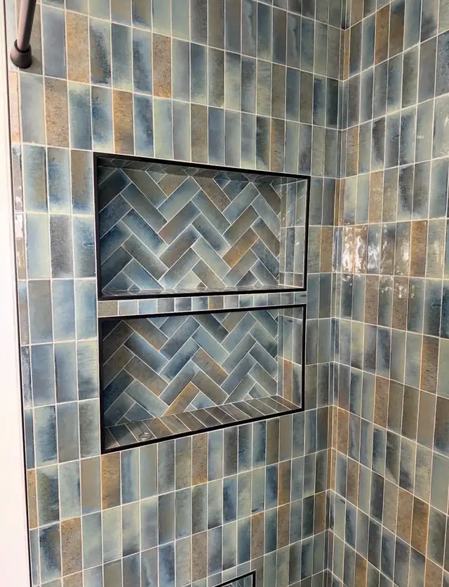 Two recessed shower niches lined with blue herringbone tile, framed in black trim on a blue glazed tile wall
