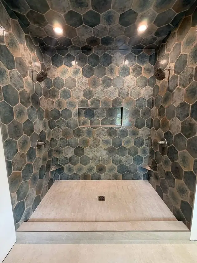 Walk-in shower with large blue-green hexagon wall tile, a recessed niche and a sand-colored tile floor with center drain