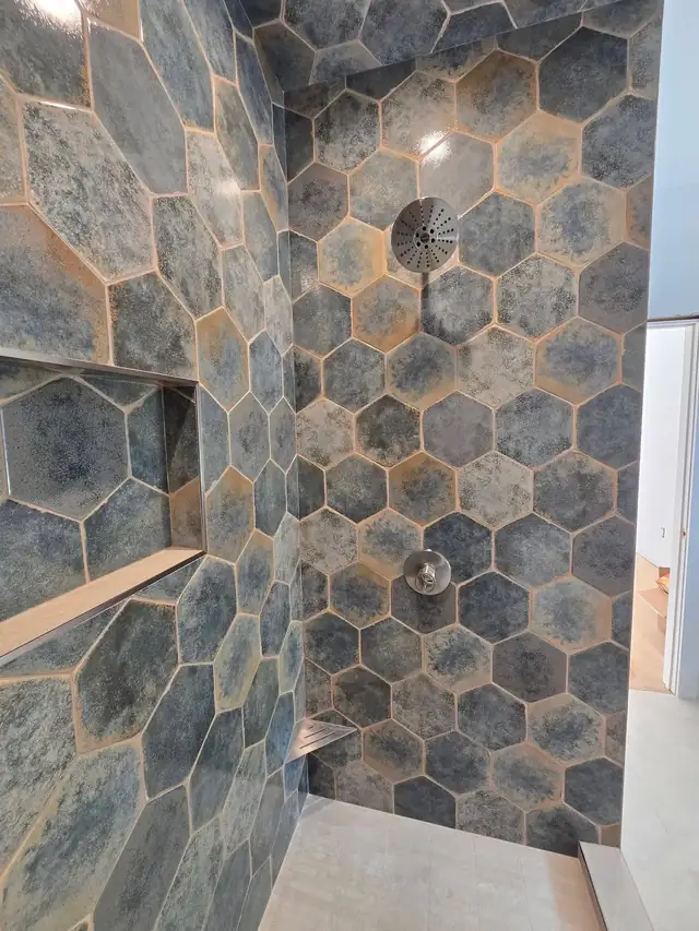 Walk-in shower by Golden Era Remodel tiled floor to ceiling in large blue hexagon tile with a recessed niche