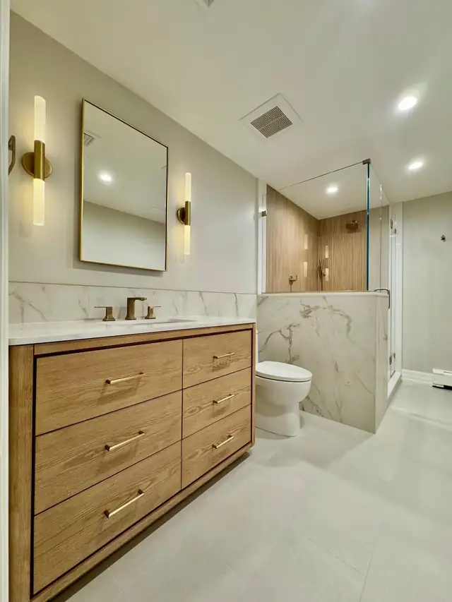 Natural oak vanity with brass pulls, white top, brass sconces and a framed mirror