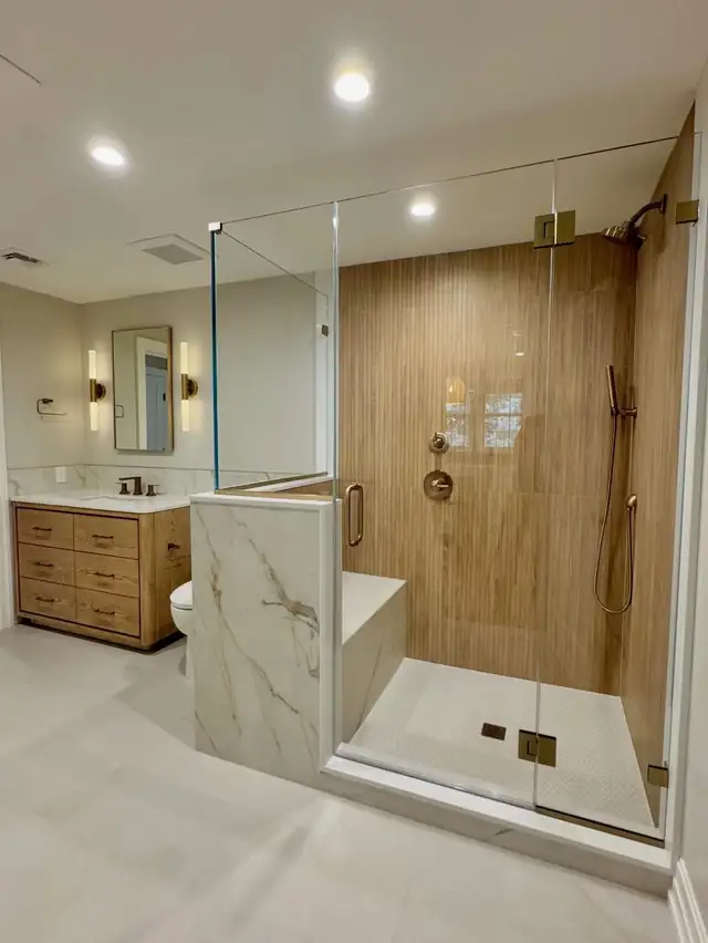 Walk-in shower with wood-look wall tile, marble-look bench and curb, frameless glass and brass hardware