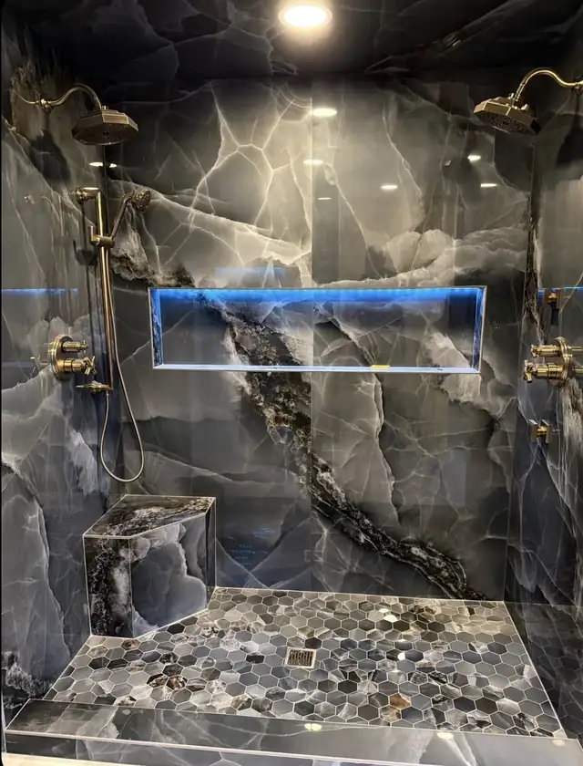 Dark onyx-look shower with lit recessed niche, corner bench, hexagon stone floor and brass dual shower heads