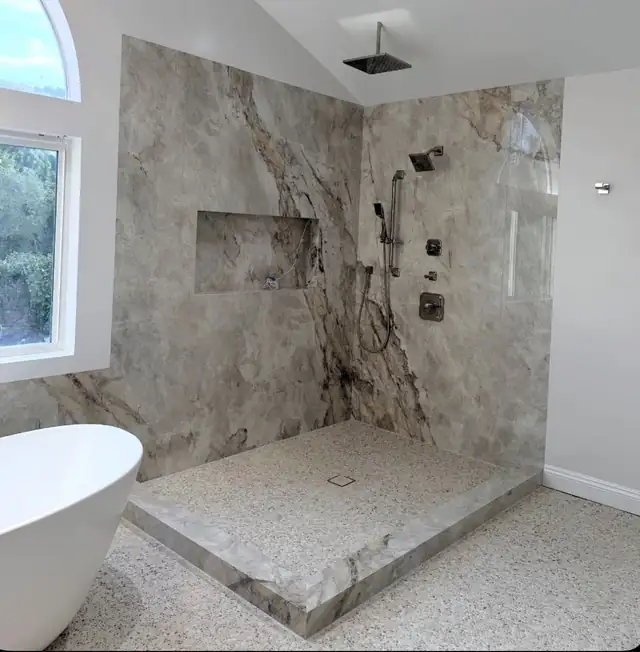 Walk-in shower by Golden Era Remodel with large-format marble-look porcelain walls, a long niche, a low marble curb and a freestanding tub under an arched window