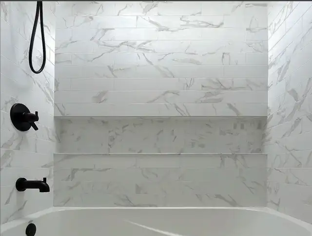 Custom tub surround in large-format marble-look porcelain with a long recessed niche and matte black fixtures